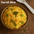 A rustic bowl of South Indian carrot rice made with grated carrots, peanuts, fluffy rice, and fresh cilantro, served on a wooden backdrop — a vibrant vegetarian lunch dish
