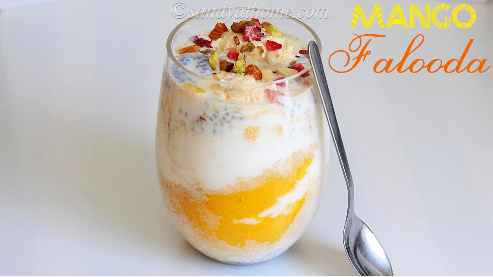 Layered mango falooda served in a tall glass with ice cream and chopped nuts