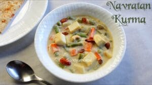 Mughlai Navratan Korma served in a bowl with creamy white gravy, paneer cubes, vegetables, cashews, and raisins, styled with saffron and nuts on top